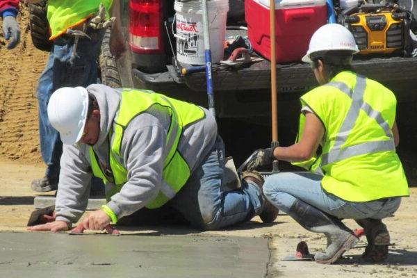 A person in safety vests and white helmets working on a concrete surface